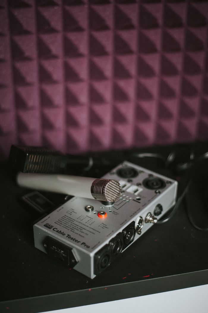 Microphone and cable tester on a studio table with soundproofing wall background.