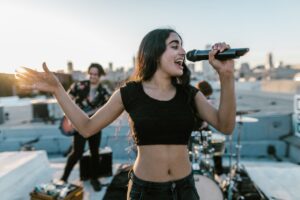 Young woman singing during a vibrant rooftop music session with band at sunset.