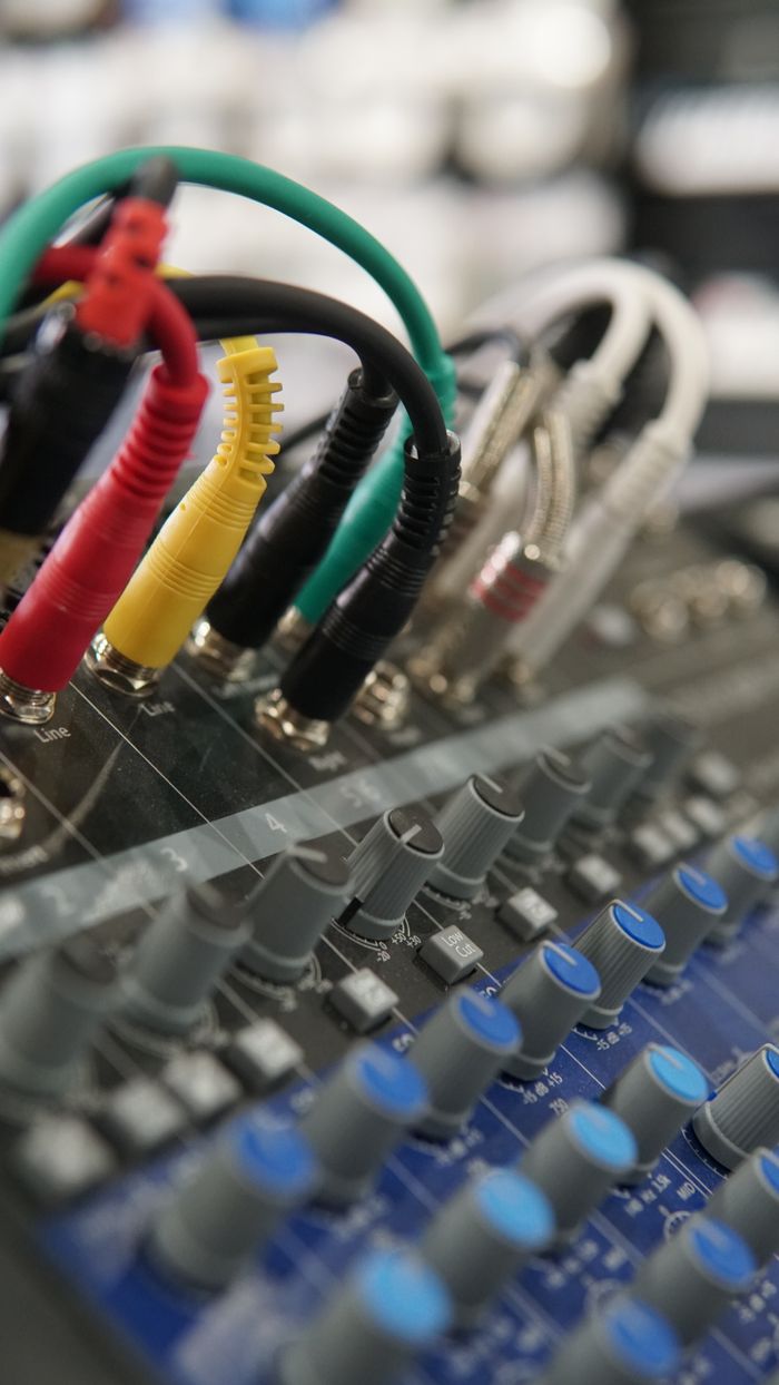 Detailed view of audio mixer controls and colorful connecting cords in a studio environment.